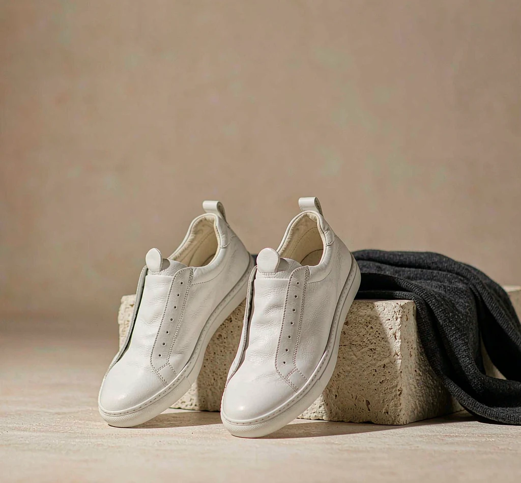 Minimalist white leather low-top sneakers beside a folded charcoal knit